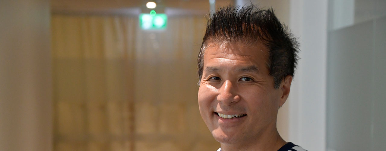 Bilden visar en man med svart hår och randig tröja. Mannen ler.