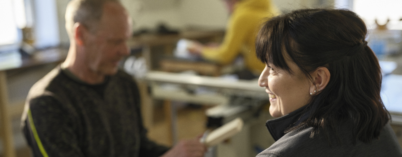 Kvinna i ett klassrum tillsammans med två andra personer som syns i bakgrunden.